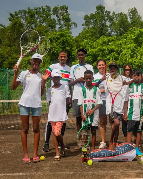 Young players of Community Tennis Suriname and their coach on their court, holding up their rackets