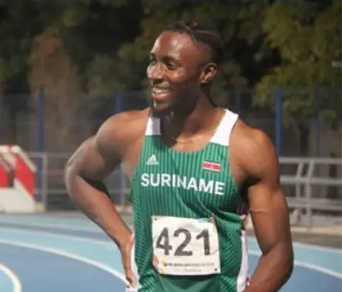 Danny Jeffrey Vanan smiling on an athletics track, wearing his Suriname racing vest