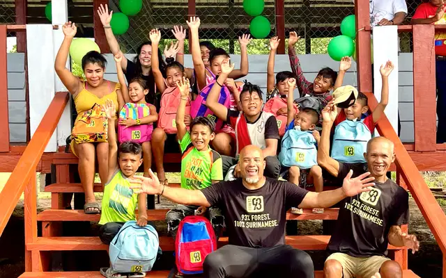 Children of Amatopo with Forest93 school bags cheering on the steps of their new school, with Dean Gorré sitting among them and green balloons tied to the railing