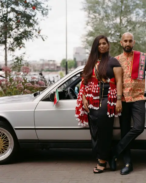Tiffany Hiralal and Rakesh Kanhai in Surinamese dress, standing beside a silver vintage car